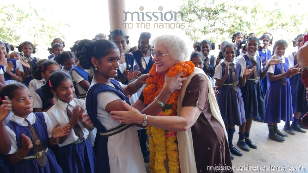 Girls welcoming an MTN visitor with a garland — the outcome when schools are reached